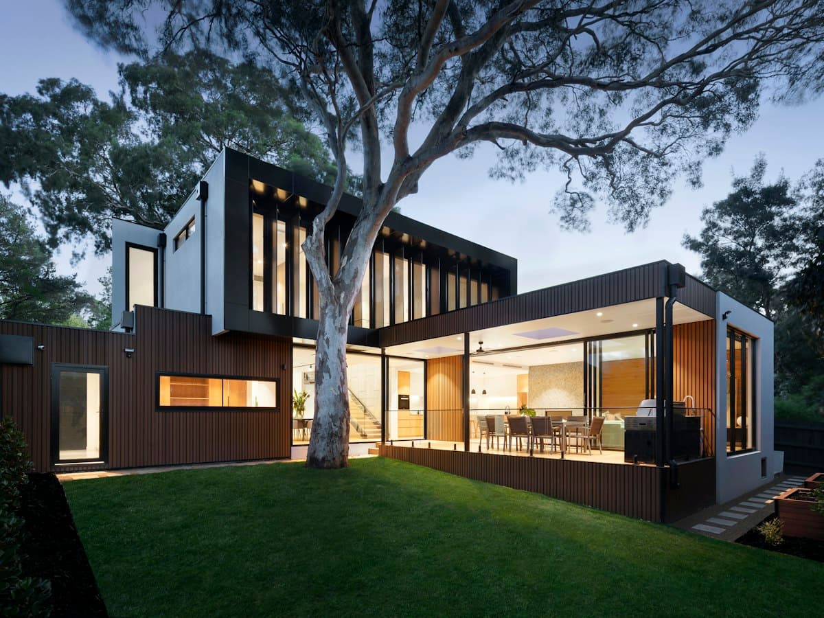 A modern house with timber walls under a large tree at dusk